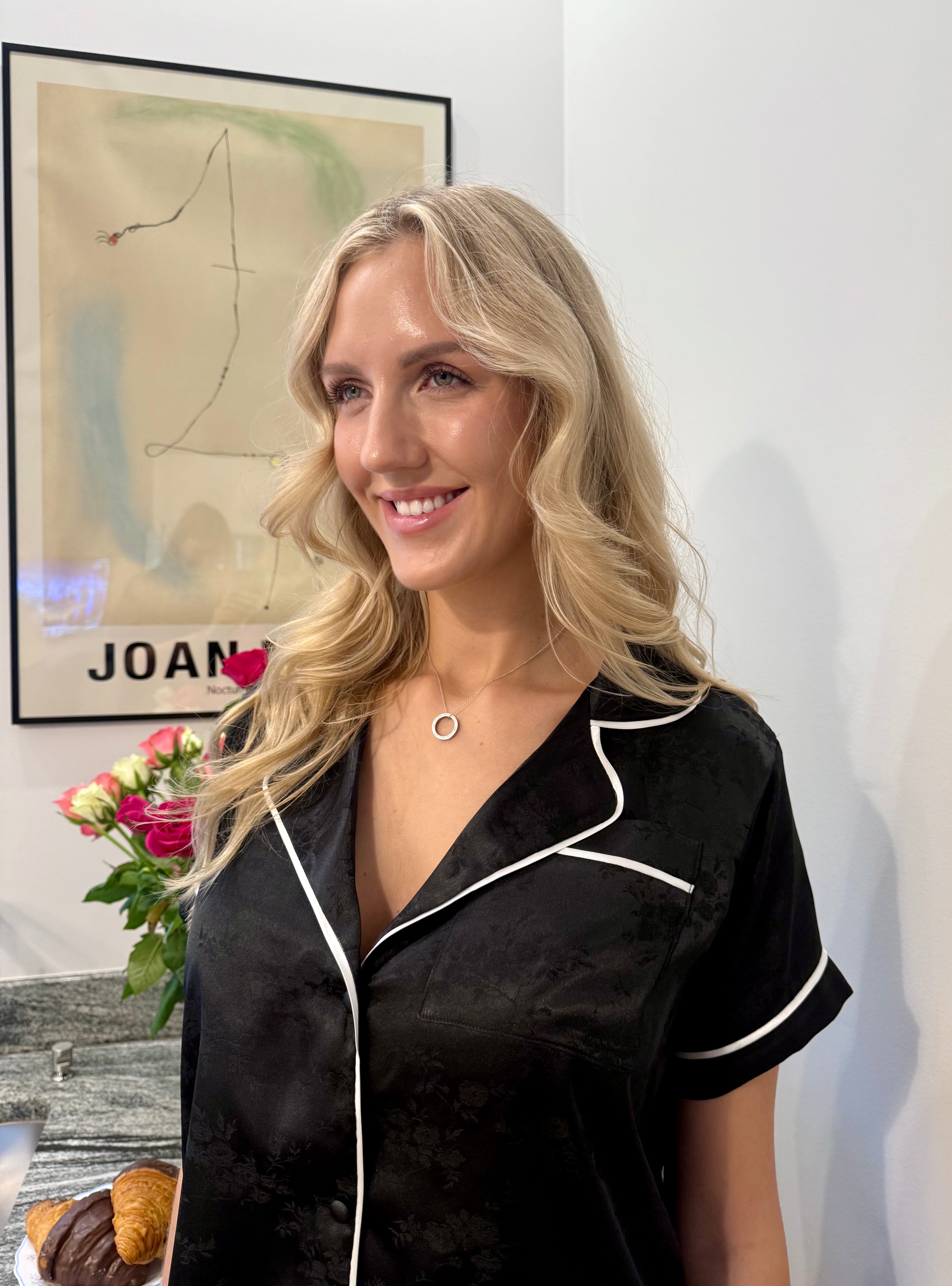 Woman wearing a black satin pajama top with white trim in a room with abstract art on the wall.